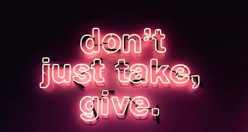 Neonlicht mit der Botschaft 'don't just take, give.' in pinker Schrift auf dunklem Hintergrund.