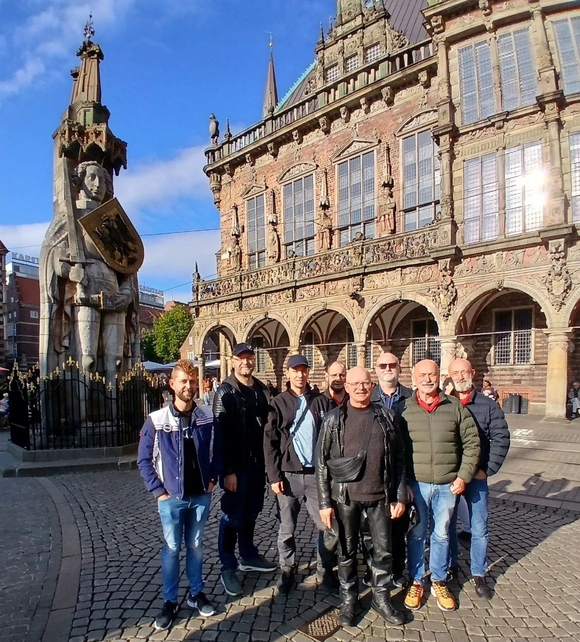 Eine Gruppe von sieben Personen posiert vor einem historischen Gebäude mit einer Statue in Bremen.